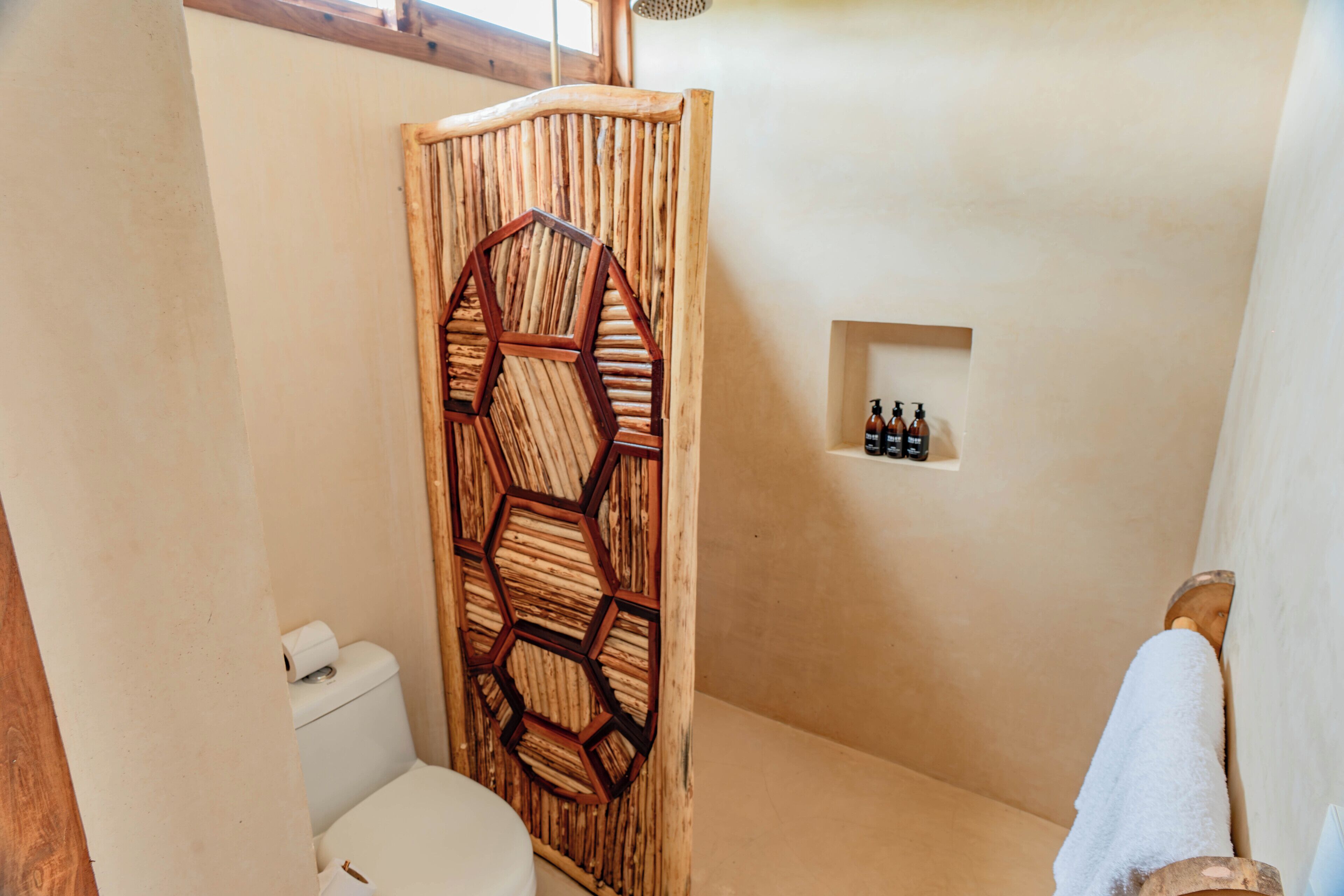 Casa de banho com cabine de duche em madeira, sanita e prateleira com artigos de higiene pessoal.