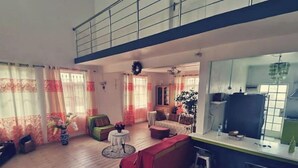 Een ruime woonkamer met een hoge plafond, een eethoek met een tafel en stoelen, en een keuken met een televisie.