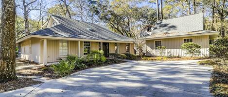 A two-story house with a front porch, surrounded by trees and a driveway.