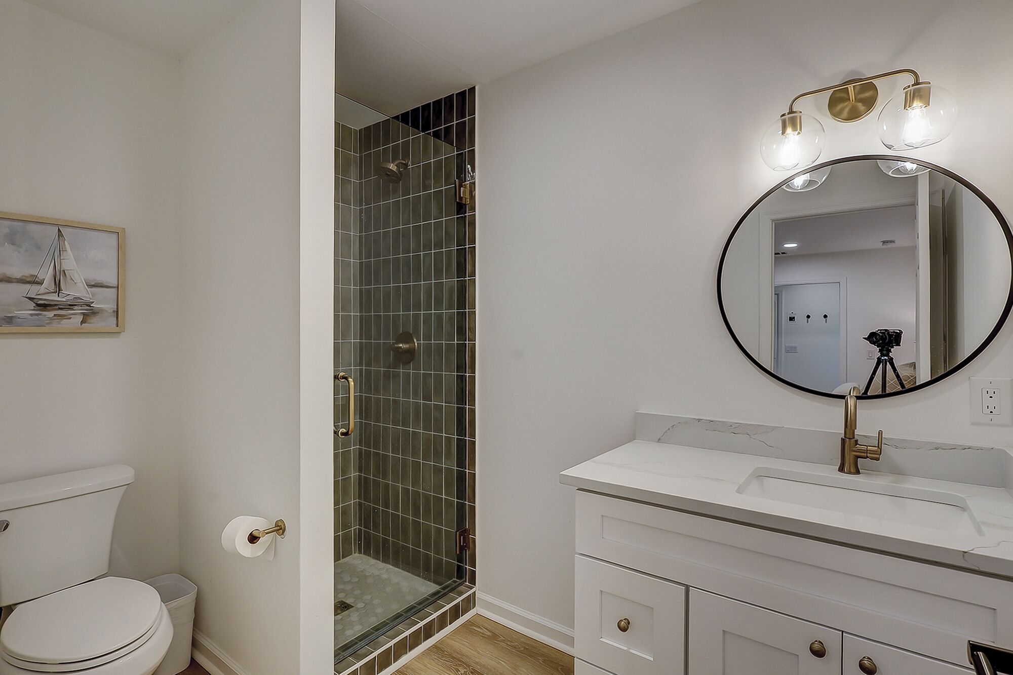 Une salle de bain comprenant des toilettes, une douche à parois de verre, un lavabo avec un miroir et un tableau encadré au mur.
