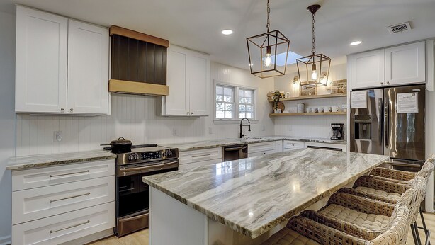 Una cocina moderna con armarios blancos, una isla grande, electrodomésticos de acero inoxidable y taburetes de bar de mimbre.