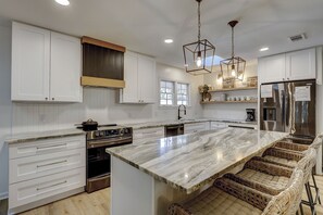 A modern kitchen with white cabinetry, a large island, stainless steel appliances, and wicker bar seating.