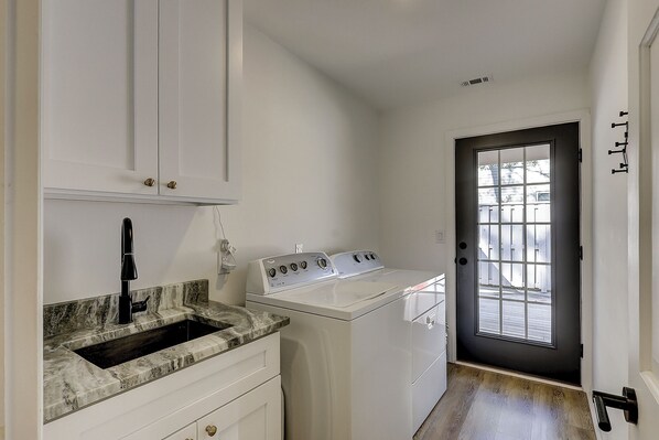 A laundry room with a sink, a washing machine, and a dryer. There is a door with a window and a doorbell.