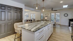Una cocina moderna con una isla de mármol, luces colgantes y vistas al área de comedor.