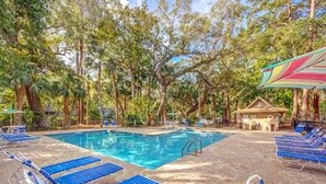 Un área de piscina con sillas reclinables azules y una pequeña estructura tipo cabaña.