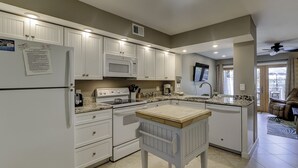 A kitchen with white cabinets, a microwave, stove, and a sink. There is a dining table with chairs. - Sunset Rentals | Continental Club 6 (HIlton Head Island)