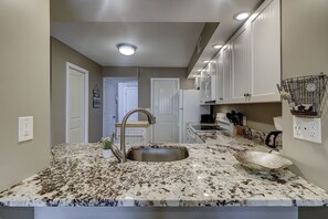 A kitchen with granite countertops, a stainless steel sink, white cabinets, and a clock on the wall.