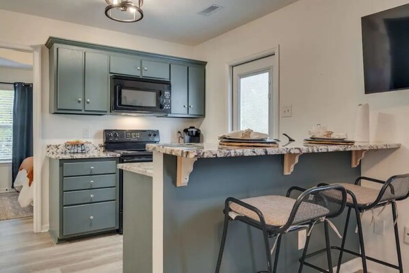 A kitchen with dark green cabinets, a black microwave, a stove, and a countertop with bar stools. - Clean and Stylishly Decorated (Lewisburg)