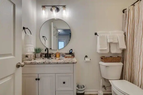 A bathroom with a round mirror, a toilet, and a shower curtain.