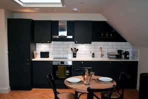 Une cuisine moderne avec des meubles de couleur sombre, des carreaux de céramique blancs rectangulaires et un coin repas comprenant une table ronde et des chaises.