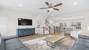 A modern living room with a flat-screen TV, a blue cabinet, a wooden coffee table, and a gray sofa. - Newly built, open-concept, and beautifully decorated 4 Bedroom in Barefoot Resort!<br>802 Dye Townhome (North Myrtle Beach)