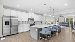 A modern kitchen with white cabinetry, stainless steel appliances, and a central island with bar stools. - Newly built, open-concept, and beautifully decorated 4 Bedroom in Barefoot Resort!<br>802 Dye Townhome (North Myrtle Beach)