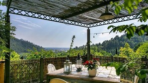 A covered outdoor seating area with a table, chairs, and potted plants.