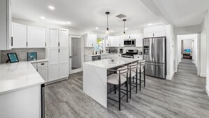 A modern kitchen with white cabinetry, stainless steel appliances, and a central island with bar stools. - Heated Pool! Kayak & Waterfront +1 Mile To Beach! (Pompano Beach)