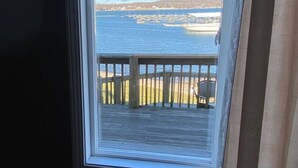 A window with a view of a waterfront, a wooden deck, and a chair. - Lakeshore-Bachelor/Bachelorette Parties welcomed! (Lake Ozark)