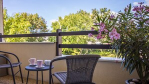Un balcon avec des fauteuils en osier, une petite table avec des tasses et un pot de fleurs orné de fleurs roses.
