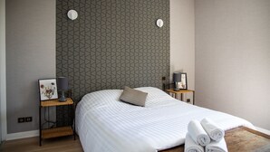 Une chambre moderne avec un grand lit, deux tables de chevet et un mur orné d’un motif géométrique.