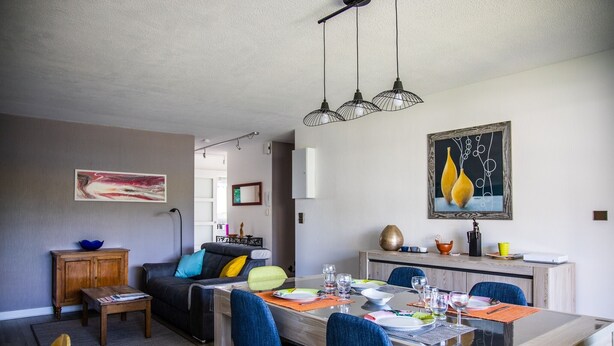 Un salon moderne avec un coin repas, comprenant une table à manger en bois, des chaises bleues et un canapé agrémenté de coussins.