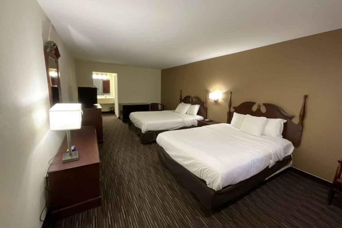 A hotel room with two beds, a desk with a lamp, and a television.