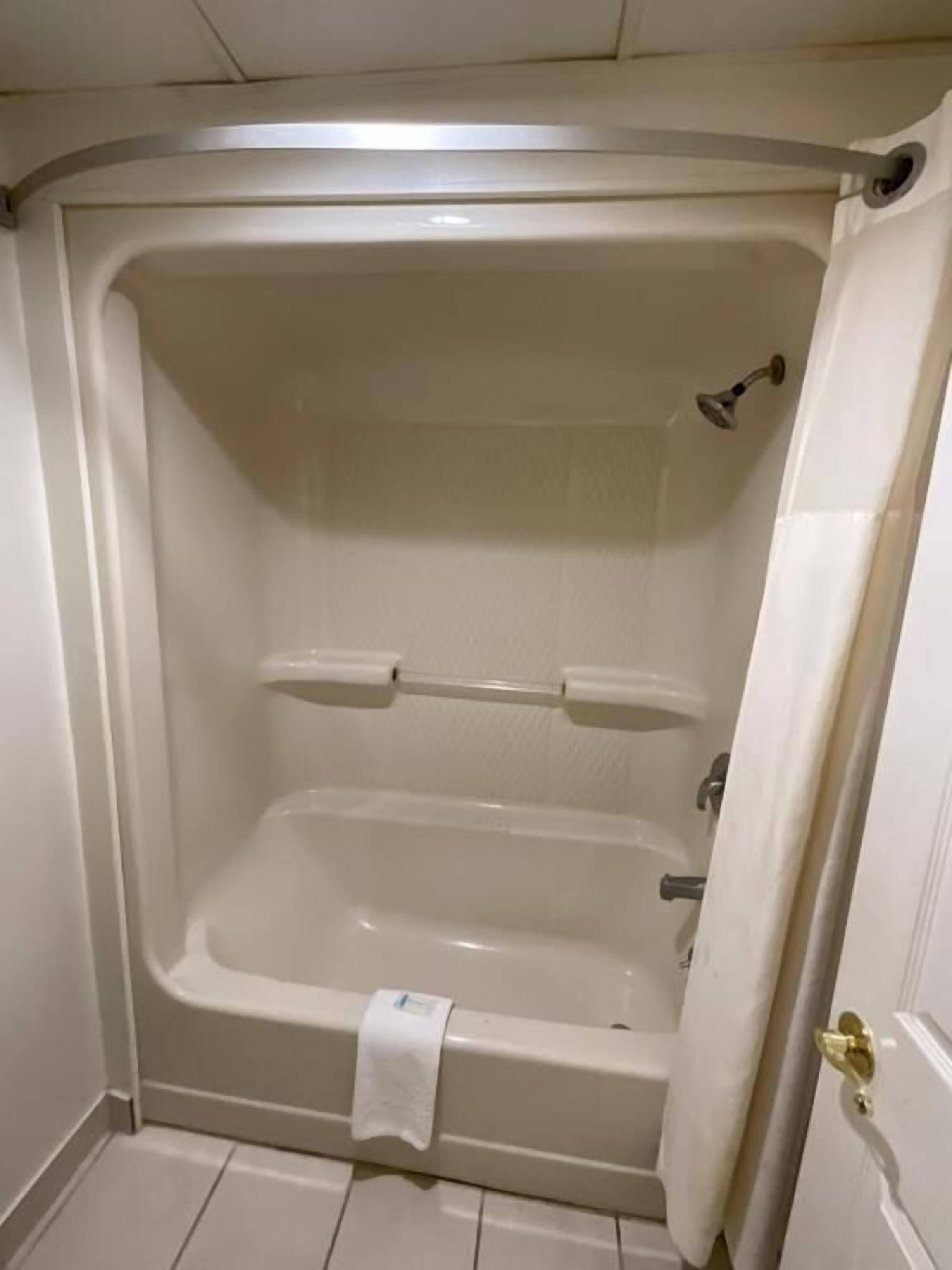 A white bathtub with a showerhead, a towel rack, and a door with a brass handle.