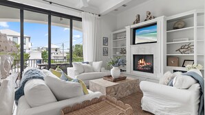 A modern living room with white furniture, a fireplace, and a large window overlooking a balcony.