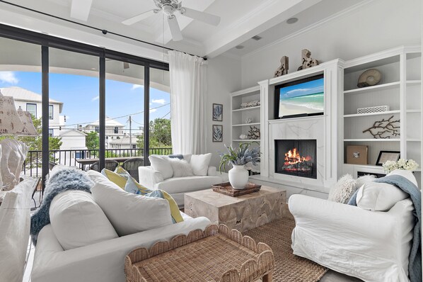 Una sala moderna con muebles blancos, una chimenea y un ventanal que da a un balcón.
