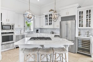 Une cuisine moderne avec des meubles blancs, des appareils en acier inoxydable, un îlot en marbre et des tabourets de bar en osier.