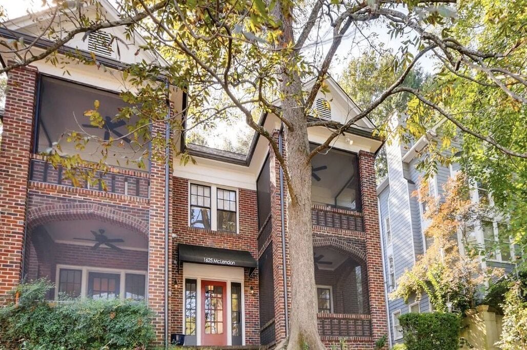 A multi-story building with brick facade, large windows, and a tree in the foreground.
