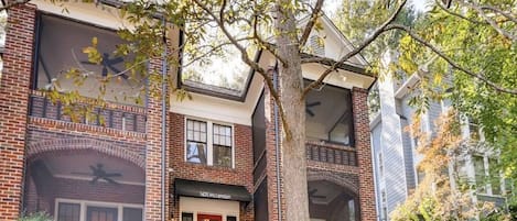 A multi-story building with brick facade, large windows, and a tree in the foreground.