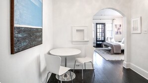 Een modern interieur met een ronde tafel en twee stoelen, een groot abstract schilderij en een doorgang naar een andere kamer.
