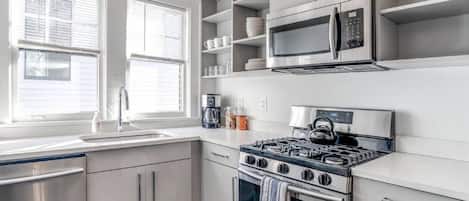 Una cocina moderna con armarios blancos, estufa de acero inoxidable, microondas y cafetera.