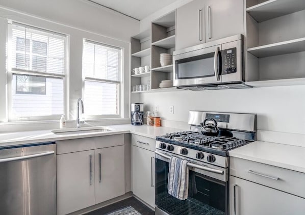 A modern kitchen with white cabinetry, a stainless steel stove, a microwave, and a coffee maker.