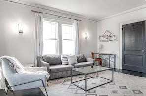 A modern living room with a grey sofa, a glass coffee table, a white armchair, and a dark door. - Historic Candler Park Gem! -Sleeps 4- Apt 3 - AC Atlanta (Atlanta)