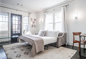 A bedroom with a bed, a chair, a rug, and a door.
