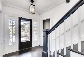 A hallway with a black door, white walls, and a staircase with white railings.