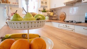 Keittiössä on hedelmäkulho, jossa on päärynöitä, banaaneja ja appelsiineja, ja se on sijoitettu puisen työtason päälle.