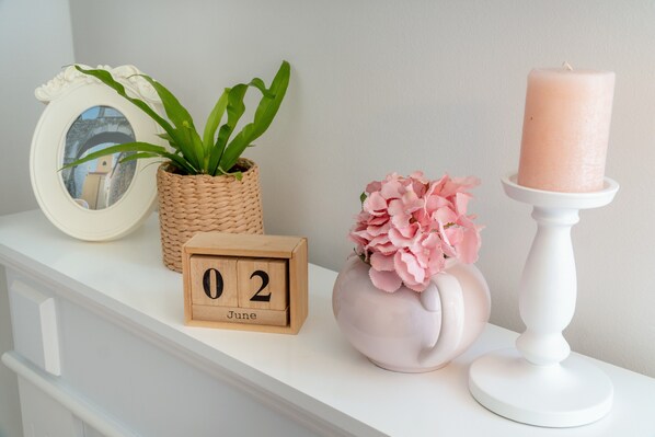A white shelf with a wooden clock, a woven plant pot, a vase with pink flowers, and a white candle holder. - Apartment for 5 persons near the main city beach (Pirovac)