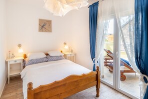 Ein Schlafzimmer mit einem hölzernen Bett, Nachttischen mit Lampen, einem Fenster mit blauen Vorhängen und einem Balkon mit einem Stuhl.