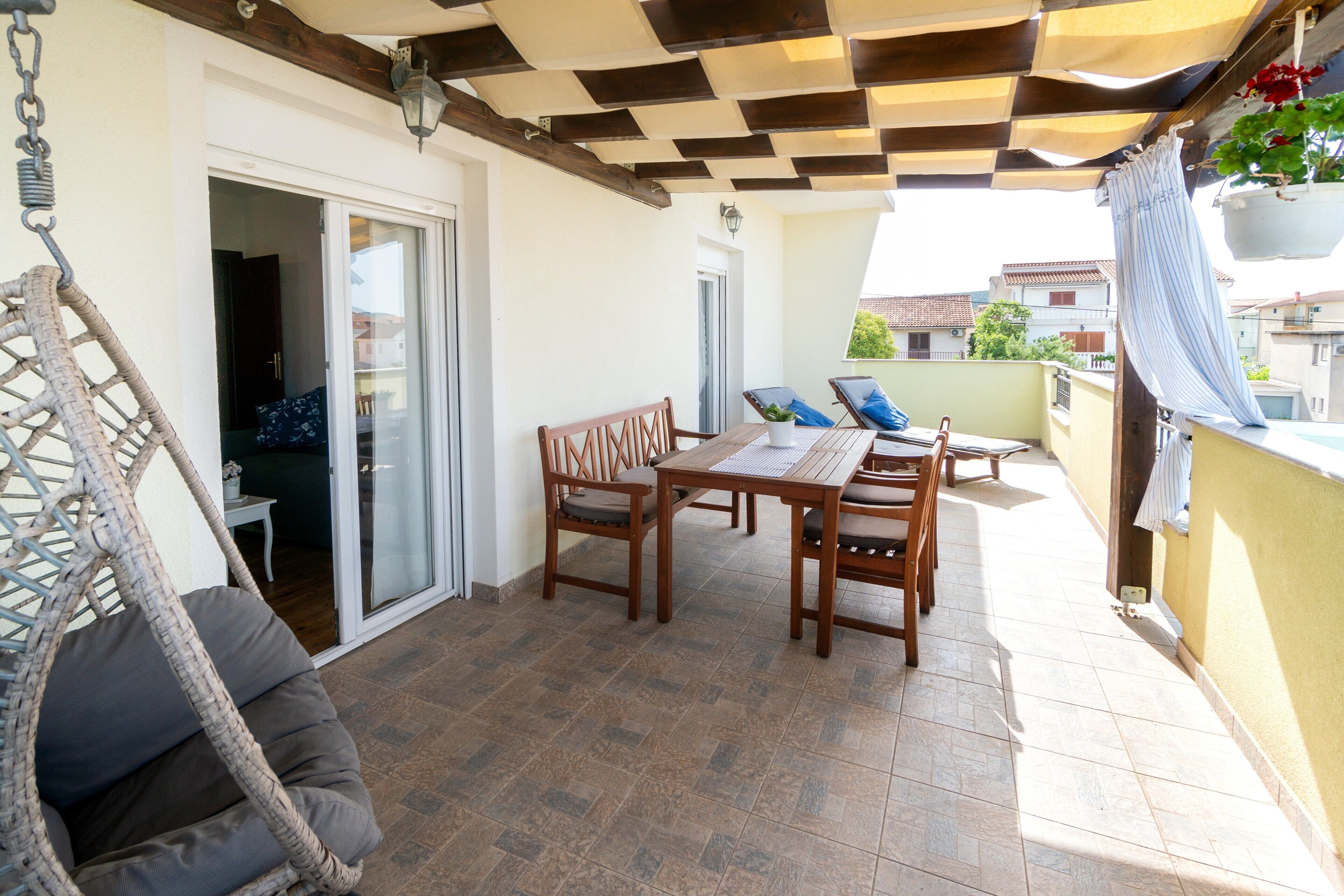 Eine Terrasse mit Tisch und Stühlen, einem Hängesessel und einem Blumentopf.