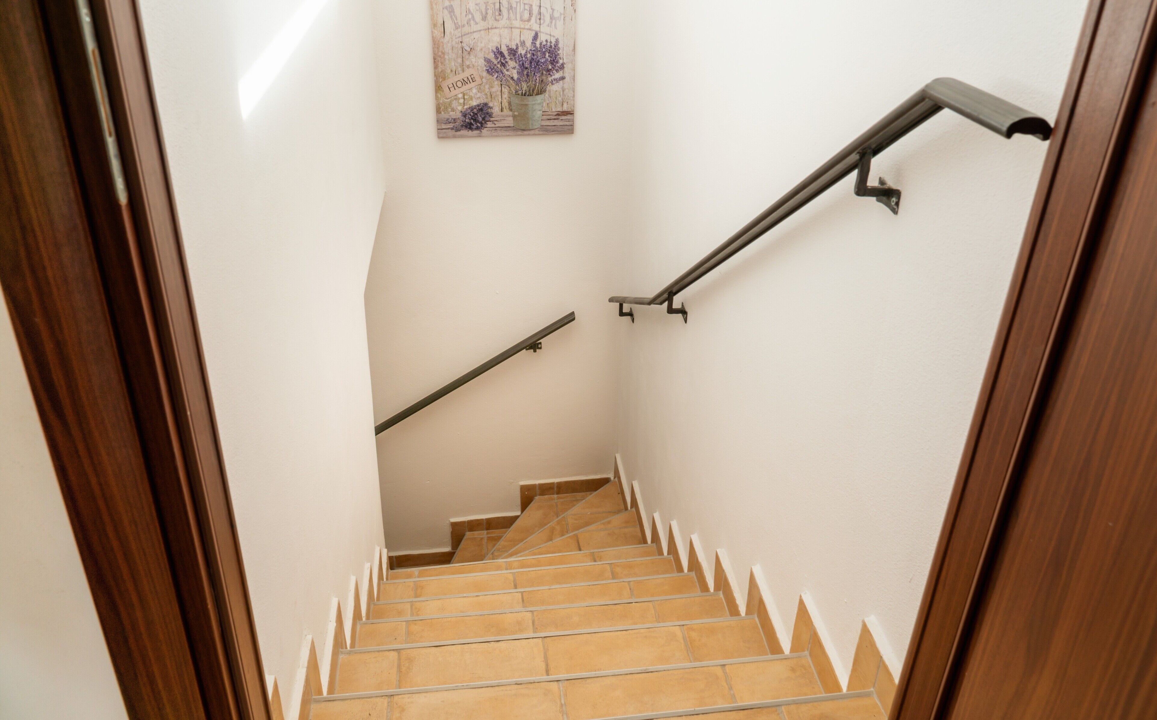 A wooden-framed staircase with beige tiles, a handrail on the right, and a decorative sign on the wall.