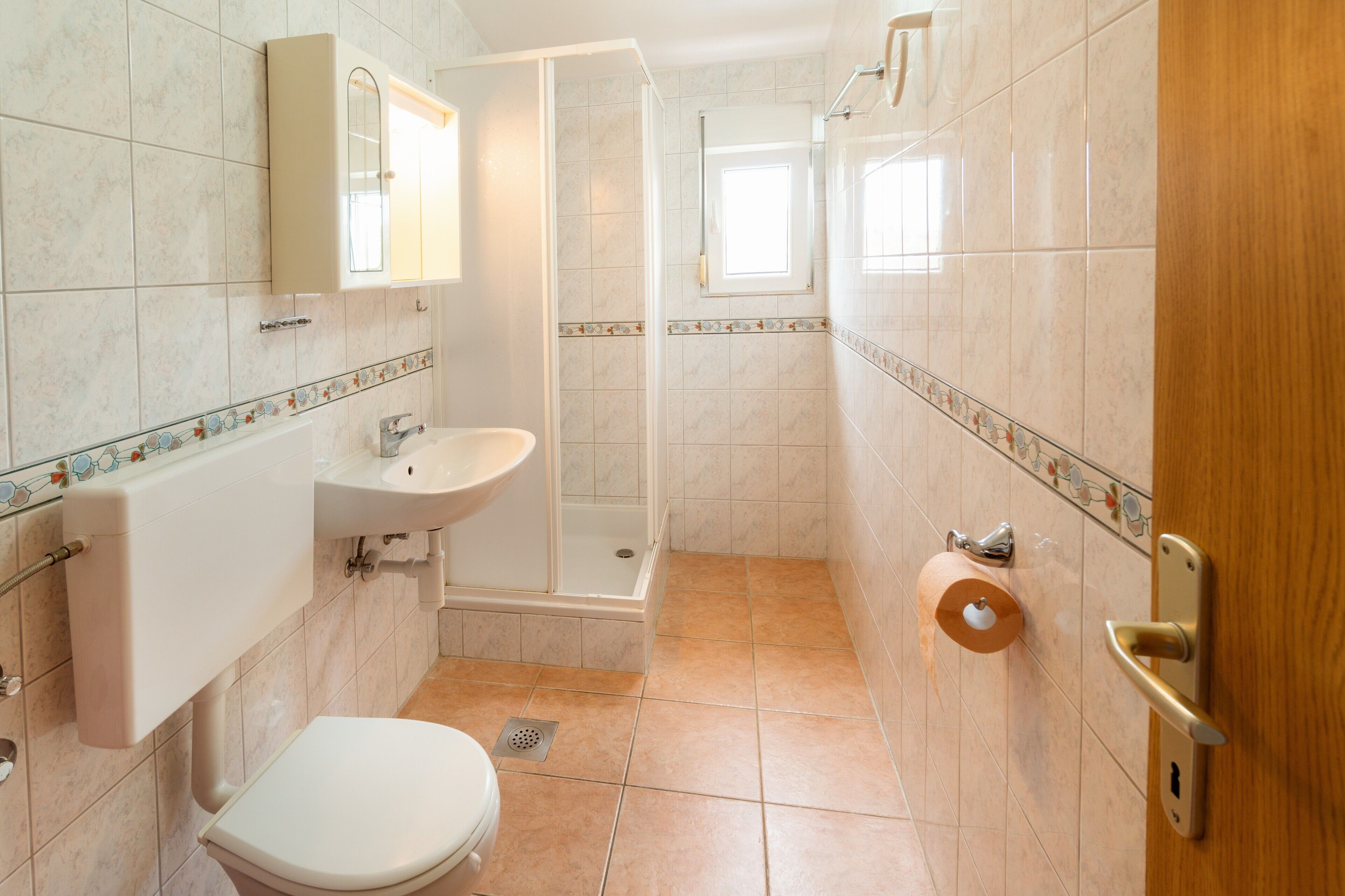 A bathroom with a toilet, sink, shower, and a toilet paper holder.