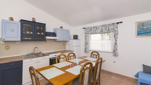 Una cocina funcional con una mesa, sillas, armarios y una ventana con cortinas.