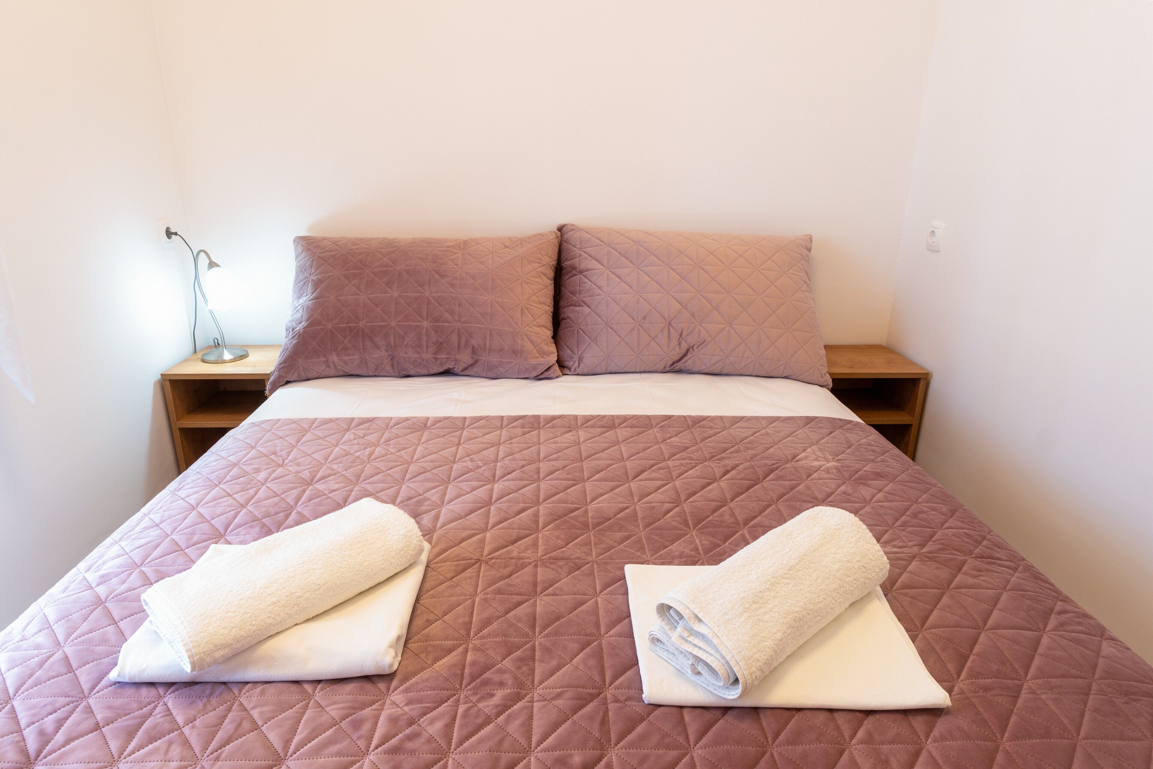 A neatly made bed with a brown quilt, two pillows, and two rolled towels on the bed.