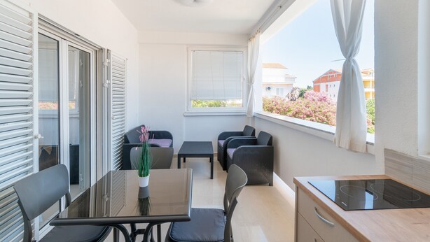 A balcony with a dining table, chairs, a small kitchen area, and a view of the neighborhood.