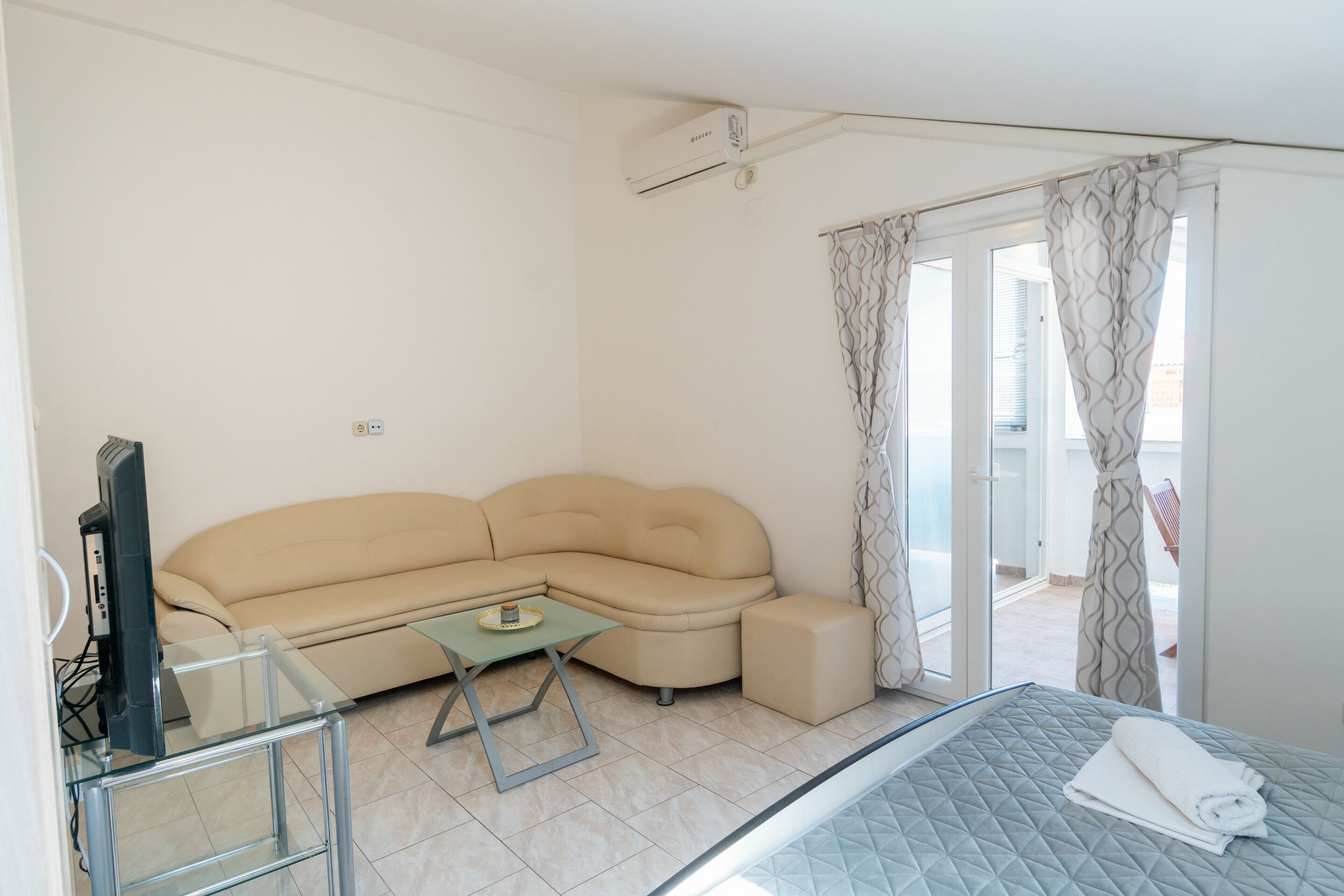 A modern room with a sofa, a glass table, a bed, and a sliding glass door leading to an outdoor area.