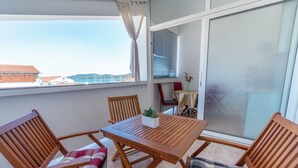Un balcon avec une table et des chaises en bois, un pot de fleurs et une vue sur des bâtiments et l’eau.