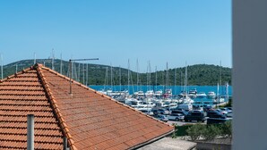 Un port de plaisance avec des voitures et des bateaux amarrés, un toit recouvert de tuiles et, au loin, un paysage vallonné.