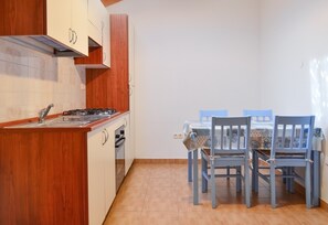 Une cuisine avec des meubles de rangement en bois, une cuisinière à gaz et une table à manger entourée de chaises bleues.