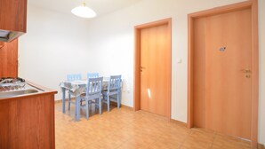 Una cocina con una mesa de comedor y sillas, un lavamanos y una estufa. Hay dos puertas de madera y una lámpara sobre la mesa.