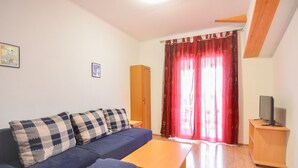 Una sala de estar con un sofá azul, una mesa de centro de madera, un televisor sobre un mueble de madera y una cortina roja.